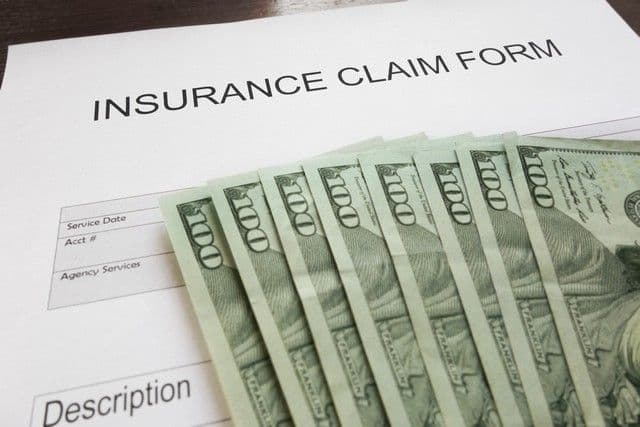 A stack of hundred-dollar bills lies on an insurance claim form. The image conveys a theme of financial reimbursement or compensation.