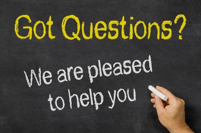 A hand writes on a chalkboard with yellow and white chalk: "Got Questions? We are pleased to help you." The tone is friendly and inviting.
