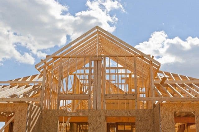 Wooden house frame under construction against a bright sky with scattered clouds. The structure conveys progress and potential in home building.