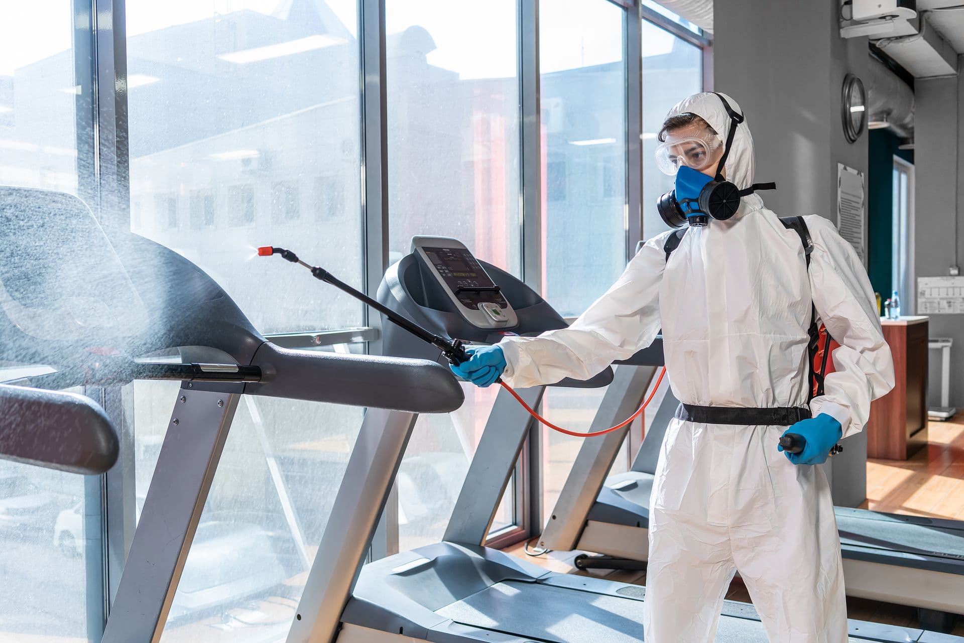 Save Download Preview professional disinfector personal protective equipment ppe suit, gloves, mask, cleaning gym space with pressurized spray disinfectant water to remove covid-19 coronavirus